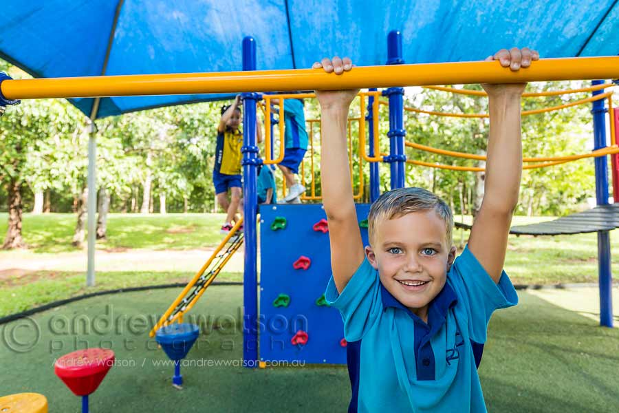 Young school boy climbing on playground equipment