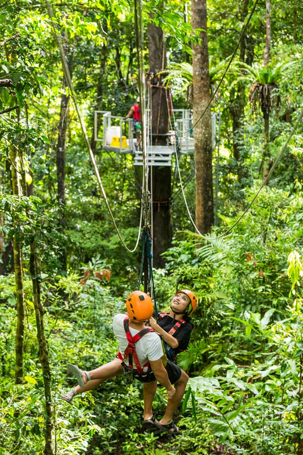 Couple moving between platforms on rainforest canopy zipline