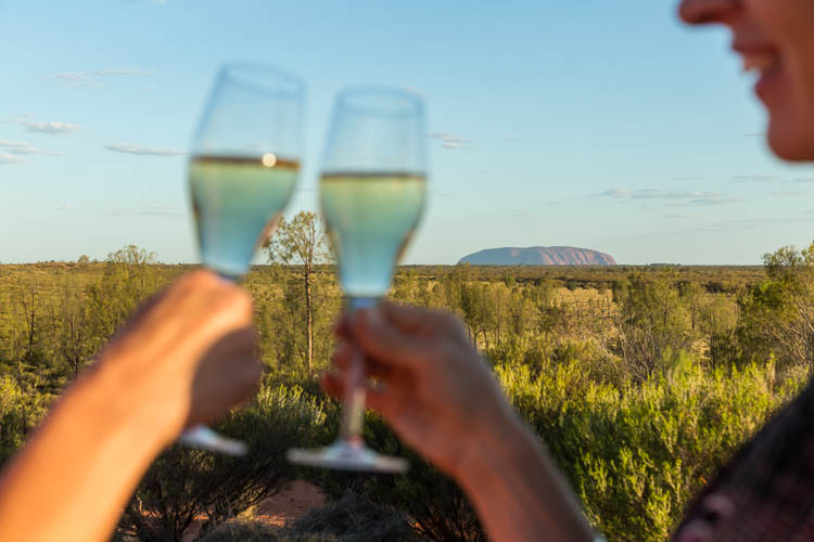 Image of guests enjoying a sunset drink with Uluru in the distance