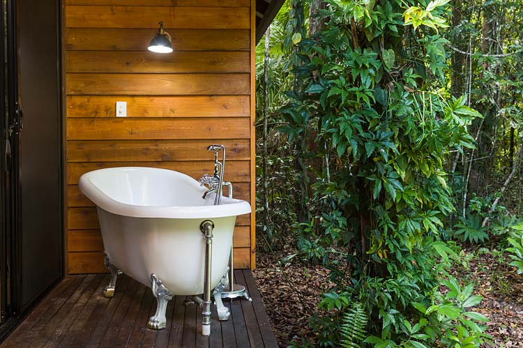 An outdoor bathtub on the deck of a holiday cottage with rainforest beyond