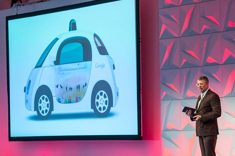 Conference speaker giving presentation on stage with image of Google car