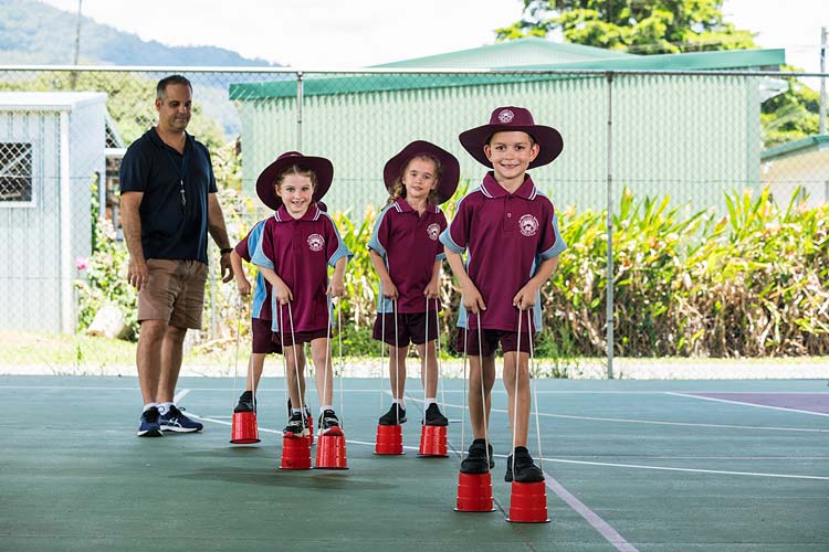 Group of school kids playing on tin-can stilts with teacher watching on