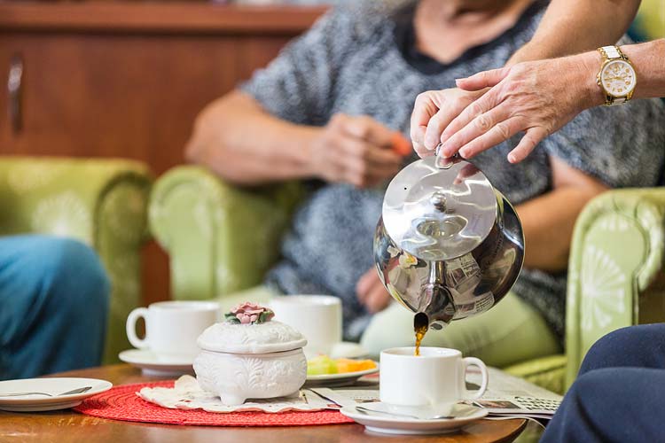 Hands of a carer pouring tea for a resident of an aged care home