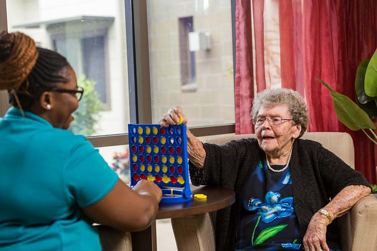 A female aged care resident enjoying a board game with her carer