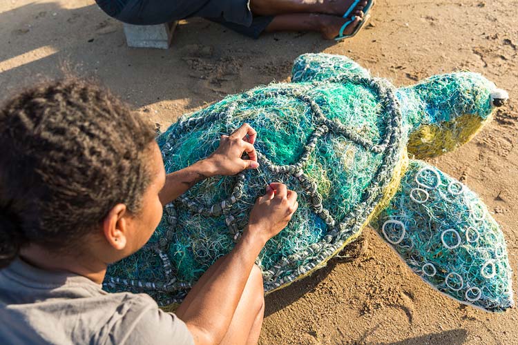 An Erub Island artist stitching a turtle artwork made from ghost net materials