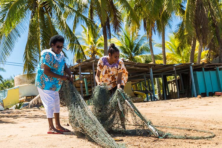 Two Erub Islander women dragging an abandoned fishing net up onto the beach