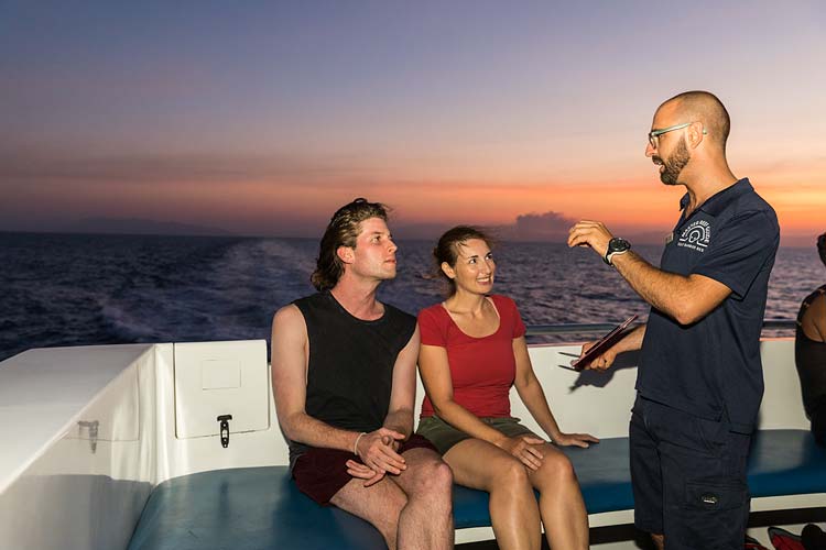 A Master Reef Guide talking to two passengers about the spawning dive on the deck of a dive vessel