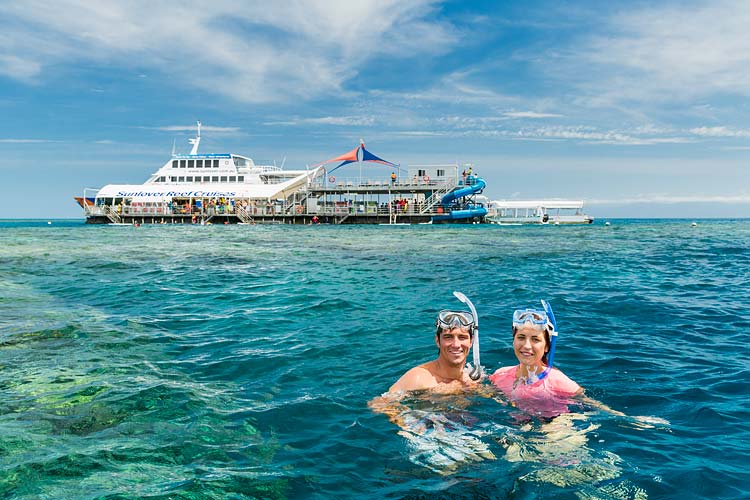 Portrait of two snorkellers in the clear waters of the Great Barrier Reef with a reef pontoon in the background