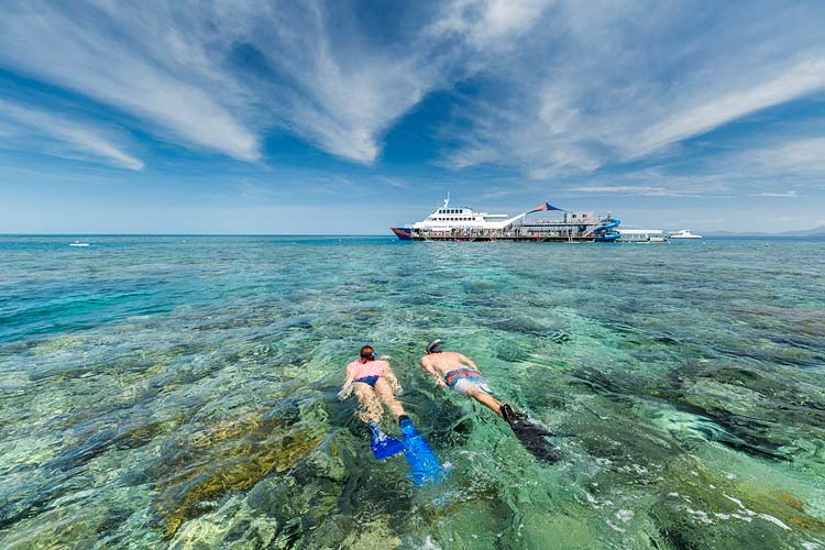 Snorkellers swimming over corals on the Great Barrier Reef with reef pontoon beyond