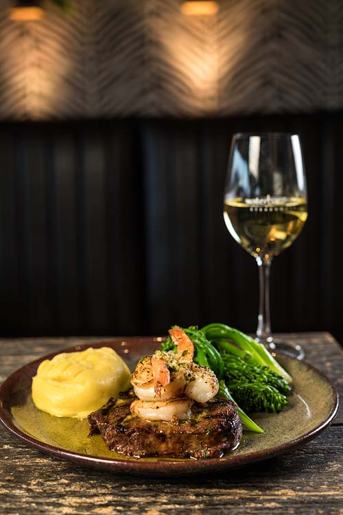 A restaurant dish of steak and prawns with garlic mash and broccolini