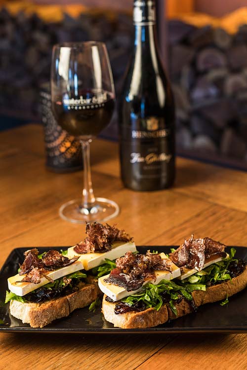 An entree dish of Brie & Biltong Bruschetta with a glass of red wine