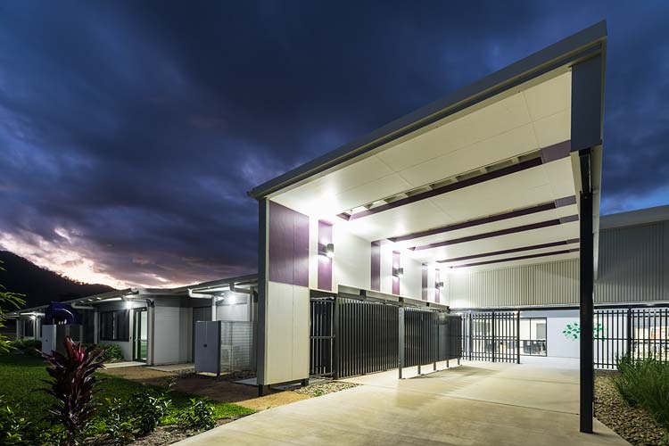 Exterior of new school building with angled roofline over entrance illuminated at twilight