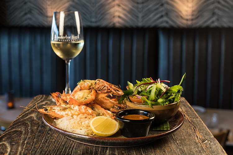 A restaurant dish of prawns, salad and glass of white wine
