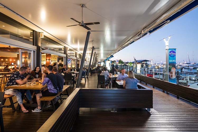 Diners on the open deck of a restaurant overlooking the marina