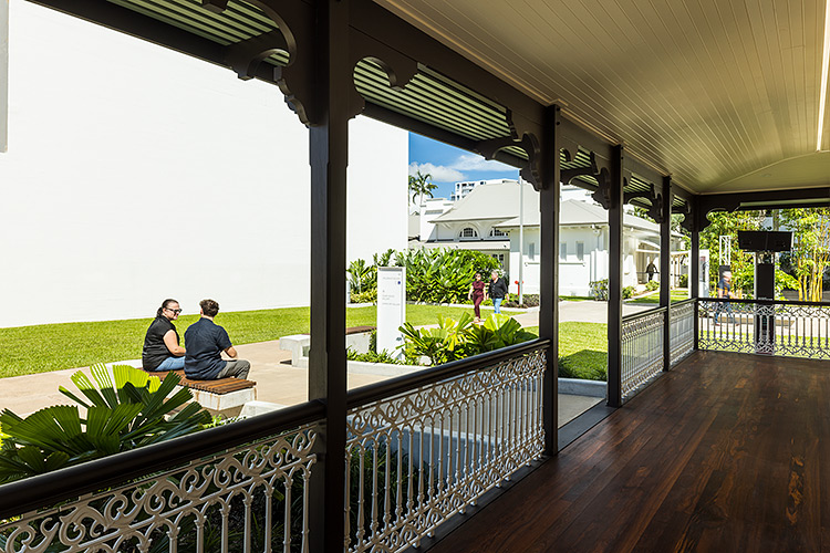 Viewing looking along building verandah to people sitting in the Mulgrave Gallery gardens