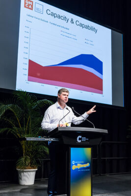 Male speaker at conference lectern with graph in background