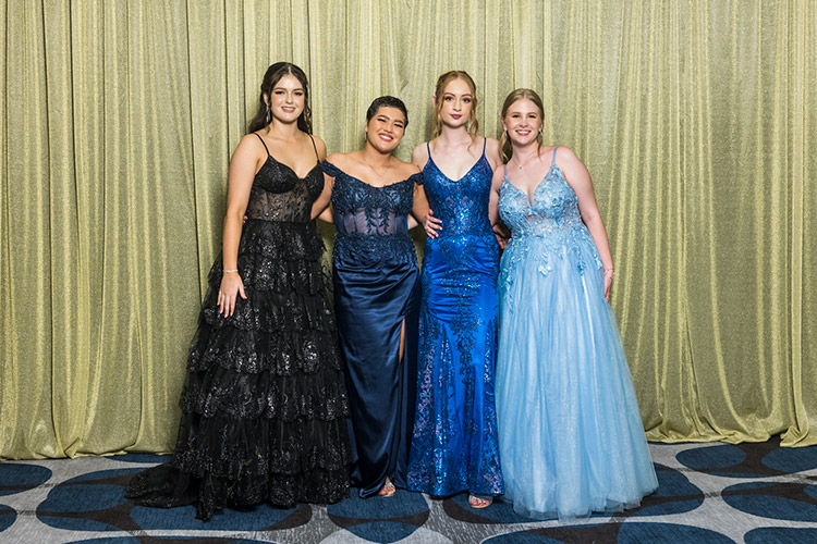 Female students at school formal photographed against a gold backdrop