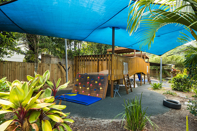 A wooden playground structure under a shade sail at an early childhood centre