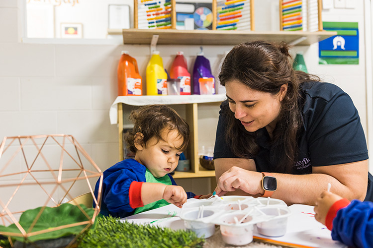 A female early childhood educator helping a toddler painting