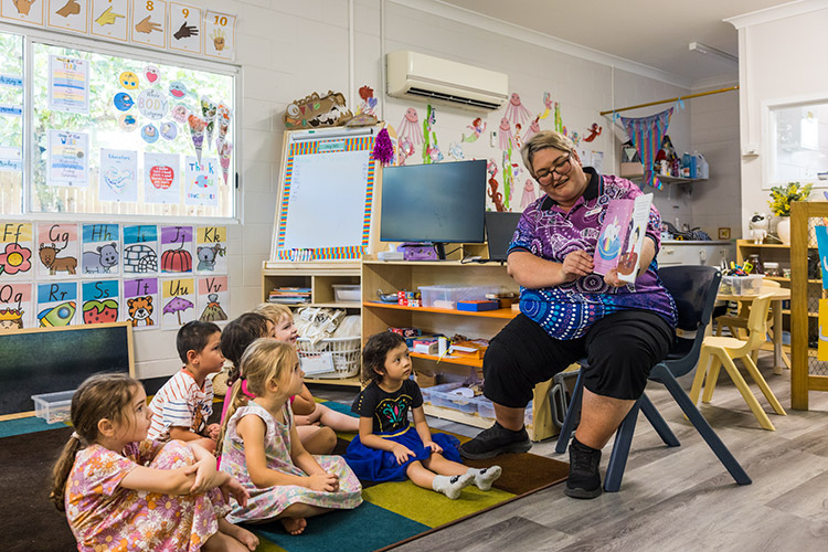 An early childhood educator reading a book to a class of young boys and girls