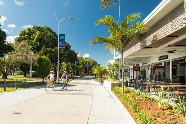 Two people cycling along roadway beside restaurant on Cairns Esplanade