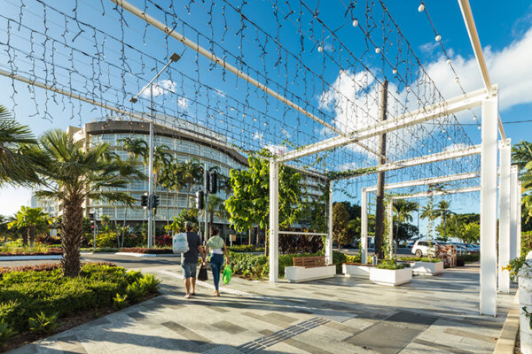 A couple walking along roadside walkway under pergola fitted with lights