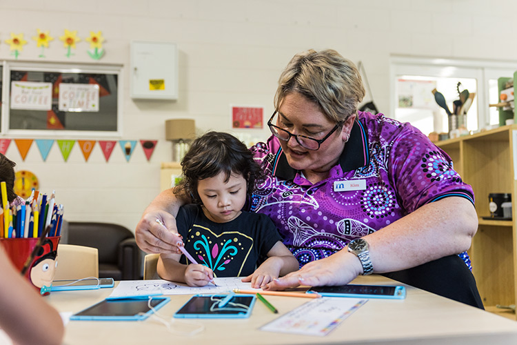 An early childhood educator assisting a young girl with colouring a picture