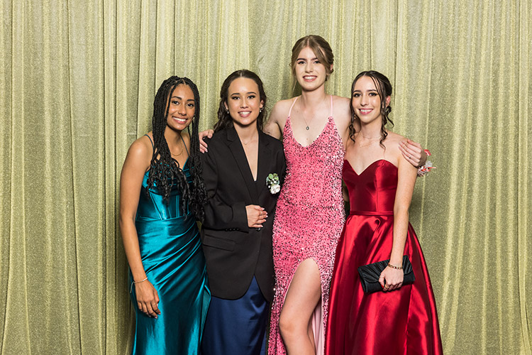 Female students at school formal photographed against a gold backdrop