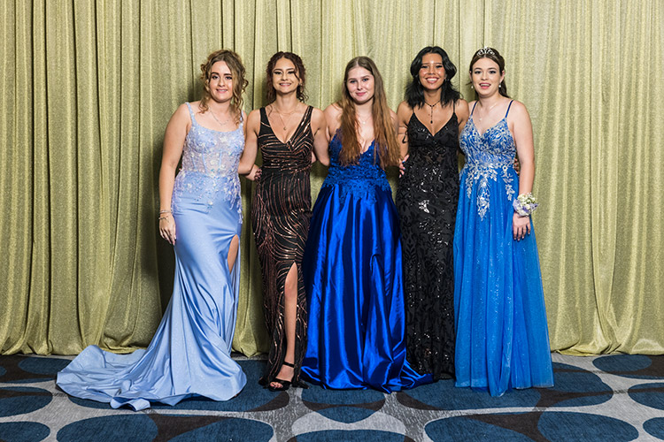 Female students at school formal photographed against a gold backdrop