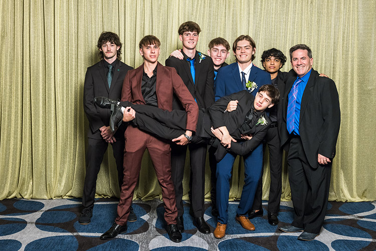 Male students and their teacher at school formal photographed against a gold backdrop